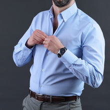 a man in a blue shirt adjusting his tie