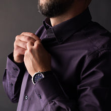 a man in a purple shirt adjusting his tie